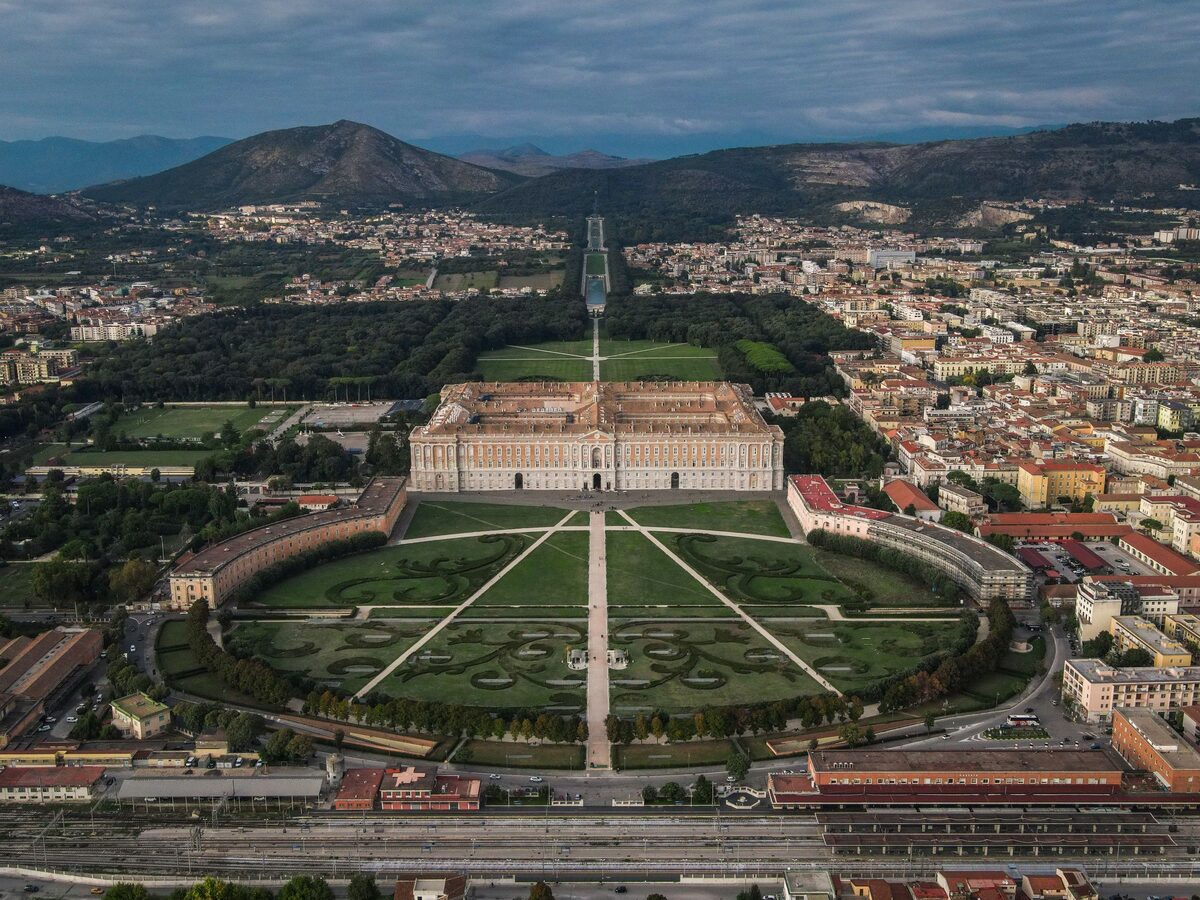 Aerial view of the vast Royal Palace of Caserta, its formal gardens and a long straight avenue of water running towards the hills