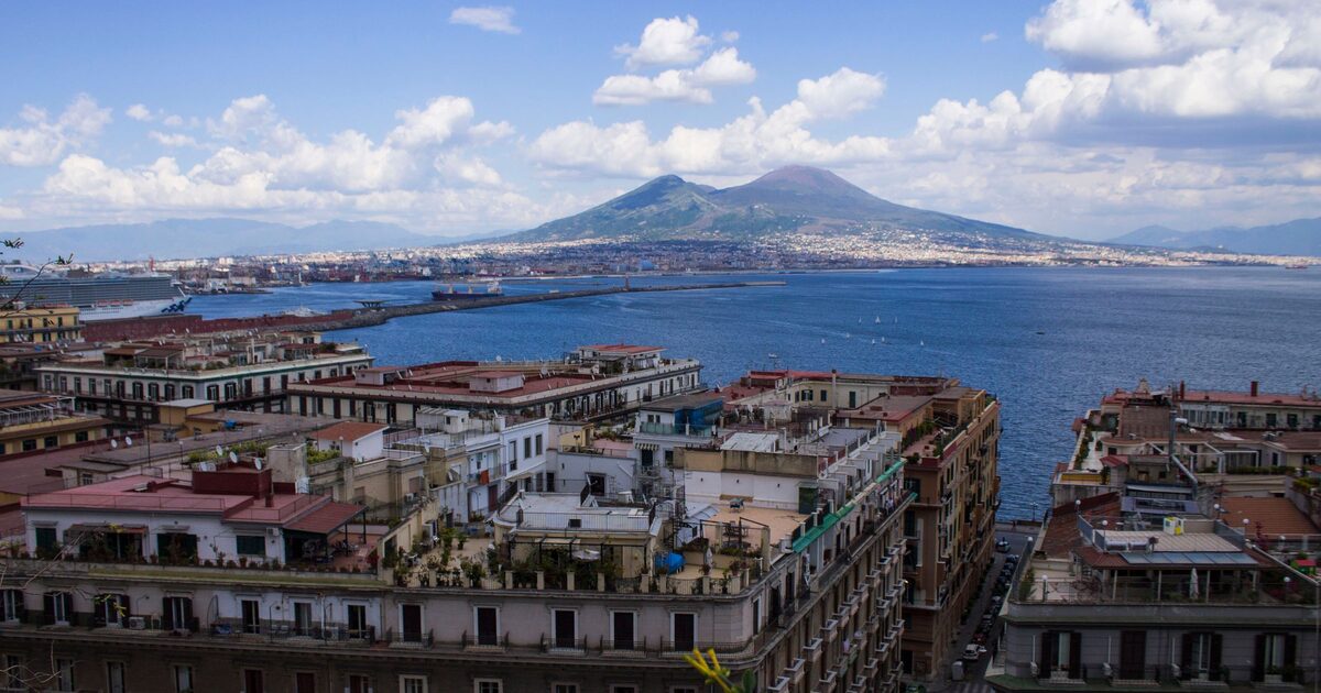 Rooftops of Naples above the harbor, with the bay and the double peak of Vesuvius under white clouds
