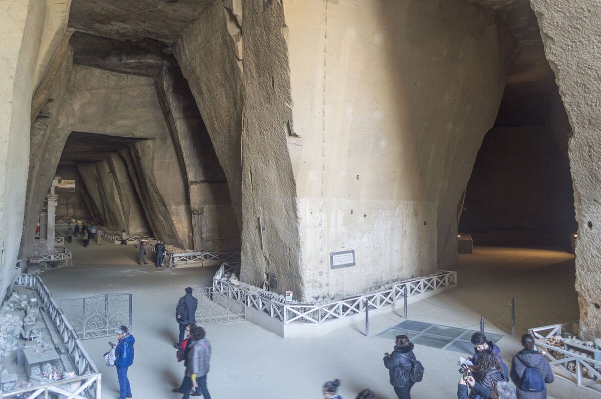 A vast tuff-stone cavern at the Fontanelle cemetery, with visitors walking between rows of stacked bones and skulls under high arches
