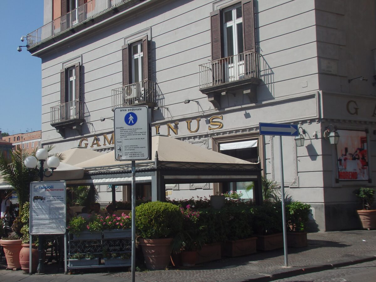The corner of Gran Caffè Gambrinus in Naples, with its gold lettering, a covered terrace and potted plants on the street