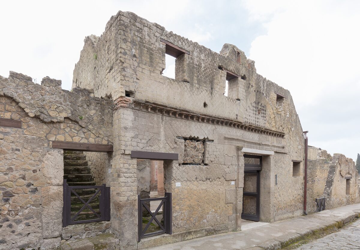 A two-story Roman house in Herculaneum with wooden balconies and doorways, its walls still standing to the upper floor