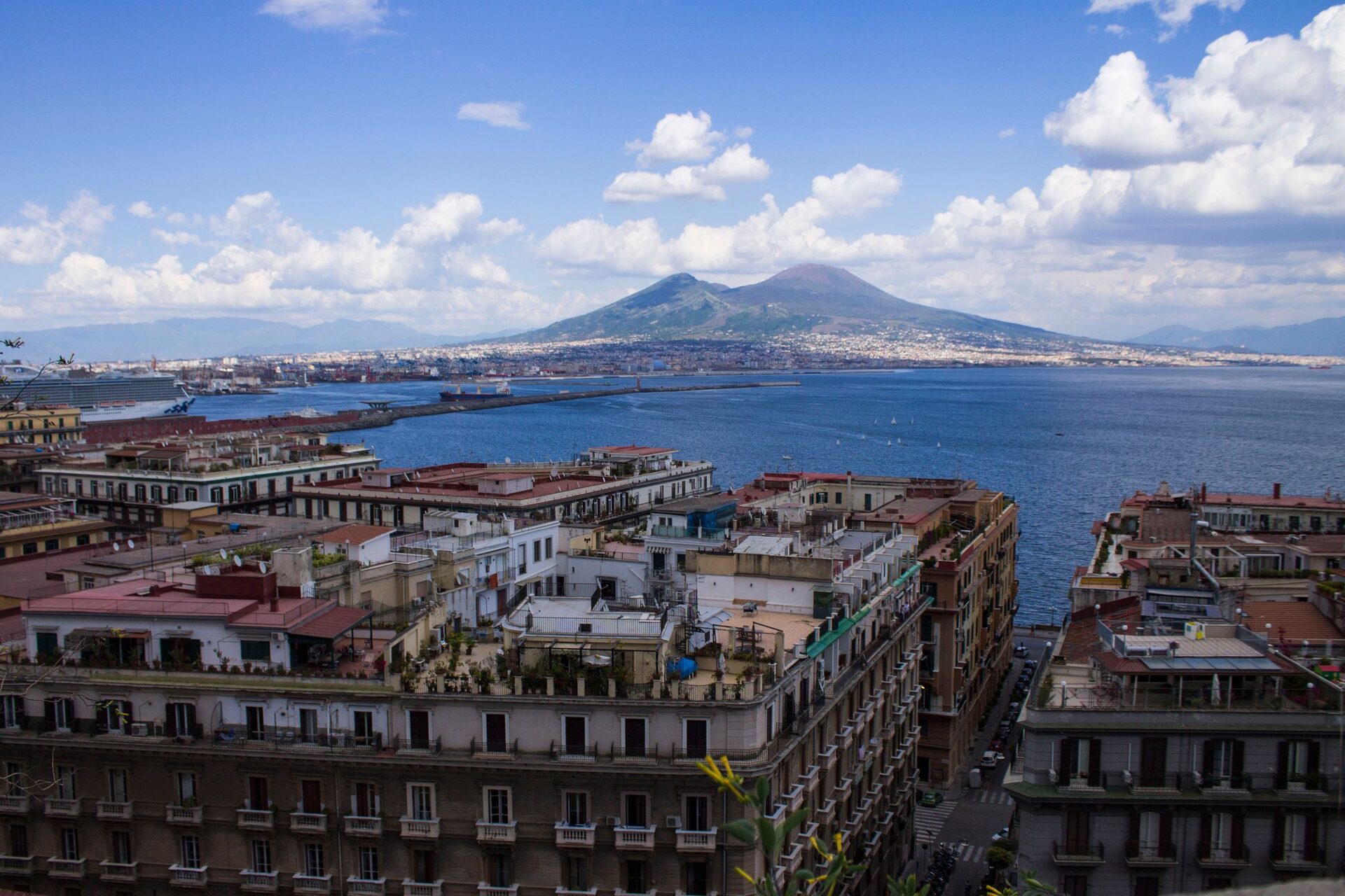 Rooftops of Naples above the harbor, with the bay and the double peak of Vesuvius under white clouds