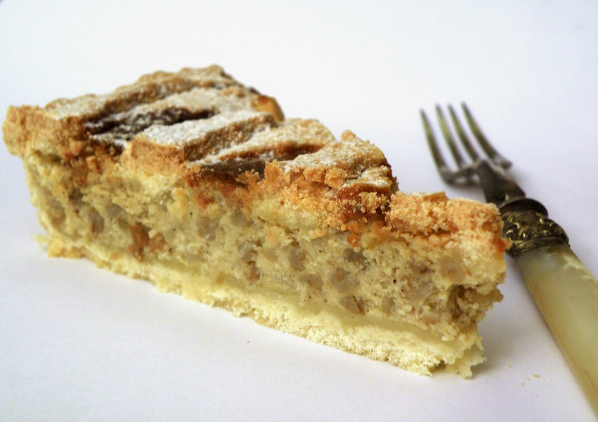 A slice of pastiera, a golden lattice-topped tart filled with ricotta and wheat, next to an old fork