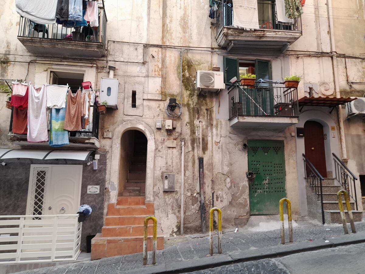 A street in the Quartieri Spagnoli with washing hanging from balconies, small doorways and steps leading up to old apartments