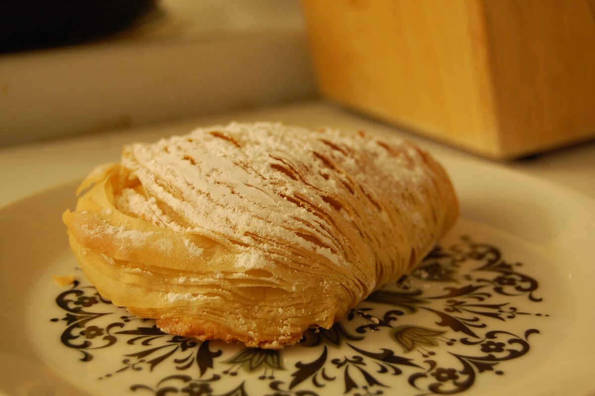 A sfogliatella riccia, a shell-shaped pastry of thin crisp layers dusted with sugar, on a patterned plate