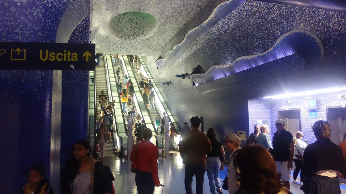 Escalators rising through the blue mosaic interior of Toledo metro station in Naples, with waves of light across the ceiling