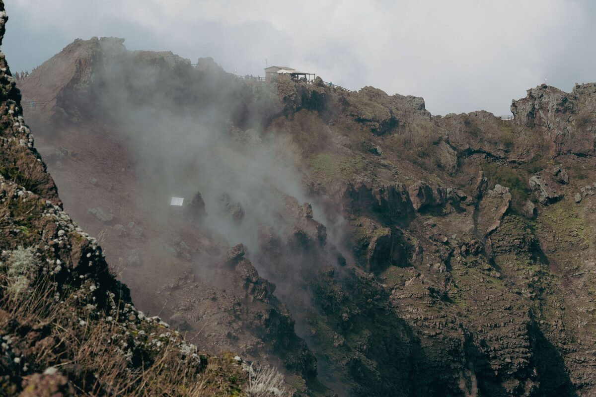 Steam rising from the steep, rocky inner wall of the crater of Vesuvius, with a small building on the rim