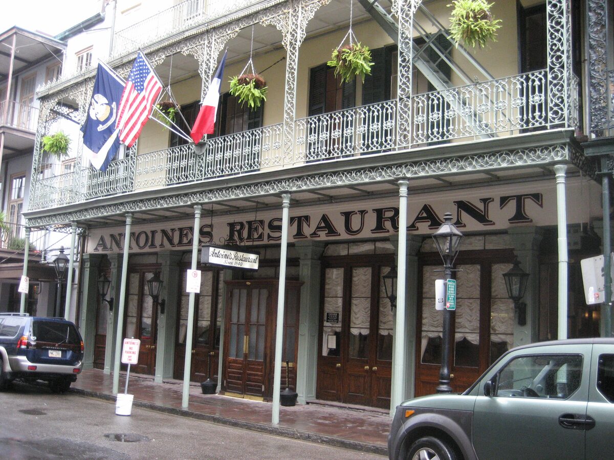 The two-level cast-iron gallery of Antoine's Restaurant on St. Louis Street with its sign, hanging ferns and flags