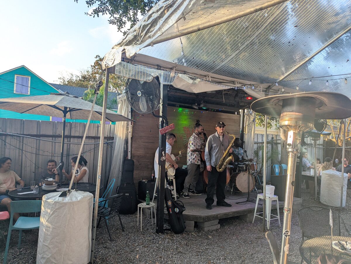 A band playing on a small stage in the covered back yard of Bacchanal, with guests at tables around it