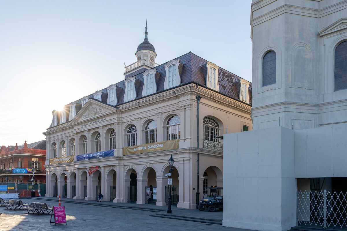 The Cabildo, a cream-colored colonial building with an arcade and a dark mansard roof beside the cathedral tower