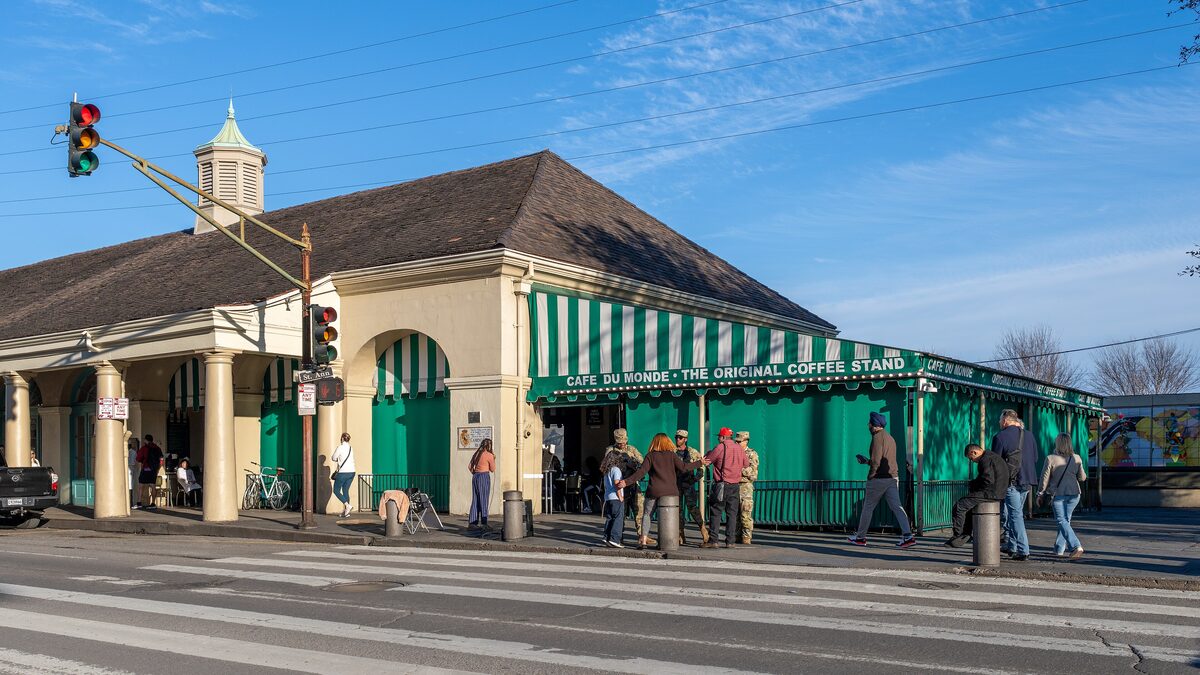The corner of Café du Monde with its green-and-white striped awning and visitors on the pavement