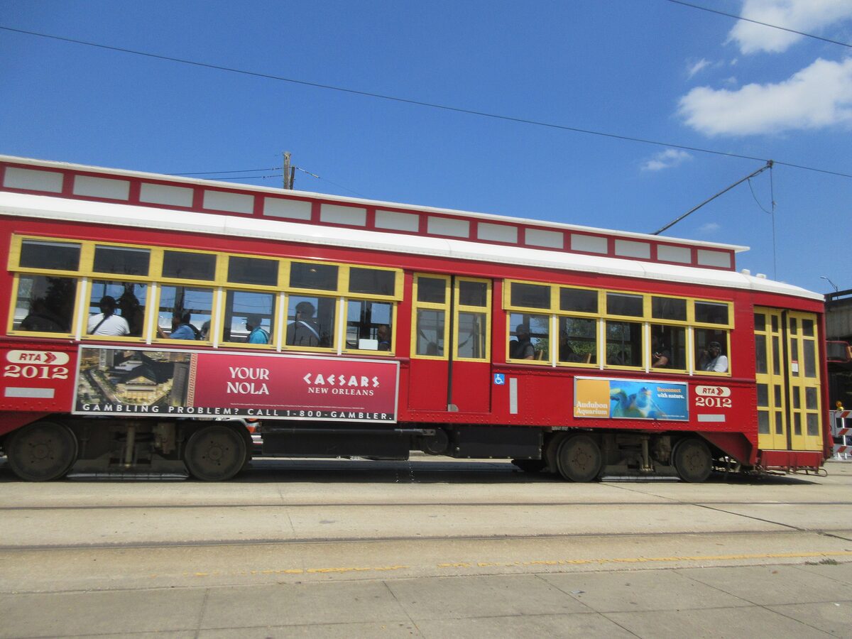A red Canal Street streetcar with yellow window frames on its track under a blue sky
