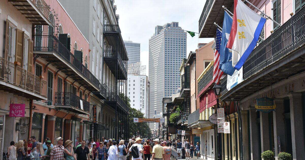 Wrought-iron balconies, flags and a gas lamp along Royal Street in the French Quarter, with downtown towers at the end of the street