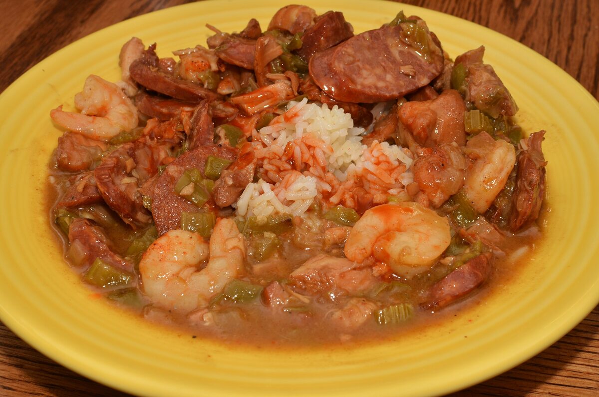 A yellow plate of shrimp and andouille sausage gumbo with a mound of rice in the middle