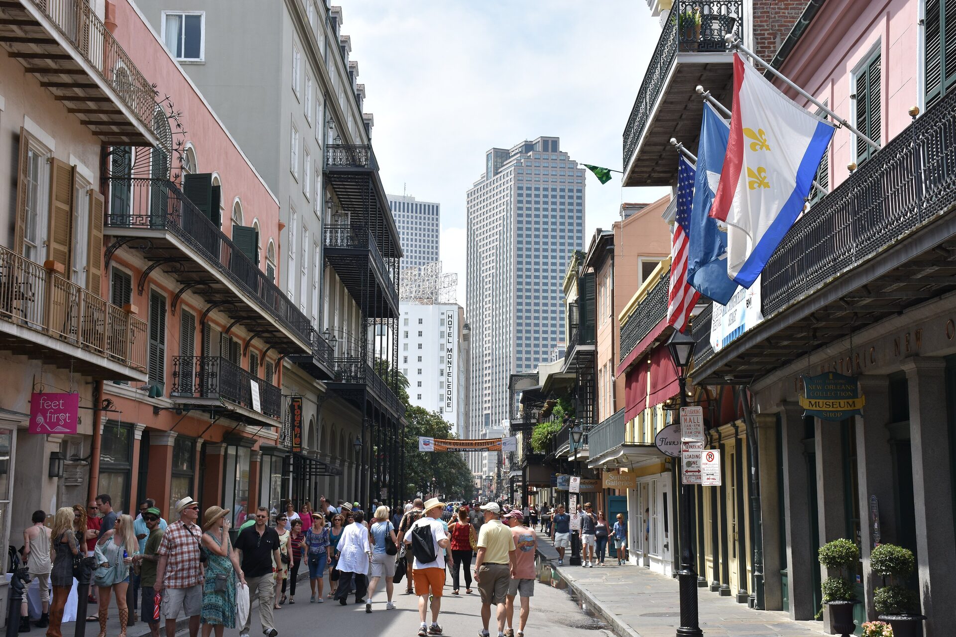 Wrought-iron balconies, flags and a gas lamp along Royal Street in the French Quarter, with downtown towers at the end of the street