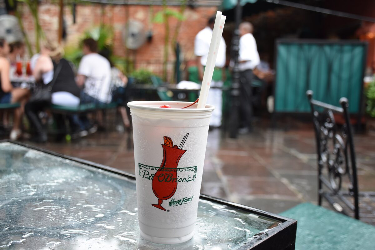 A Hurricane cocktail in a Pat O'Brien's cup with a straw on a patio table