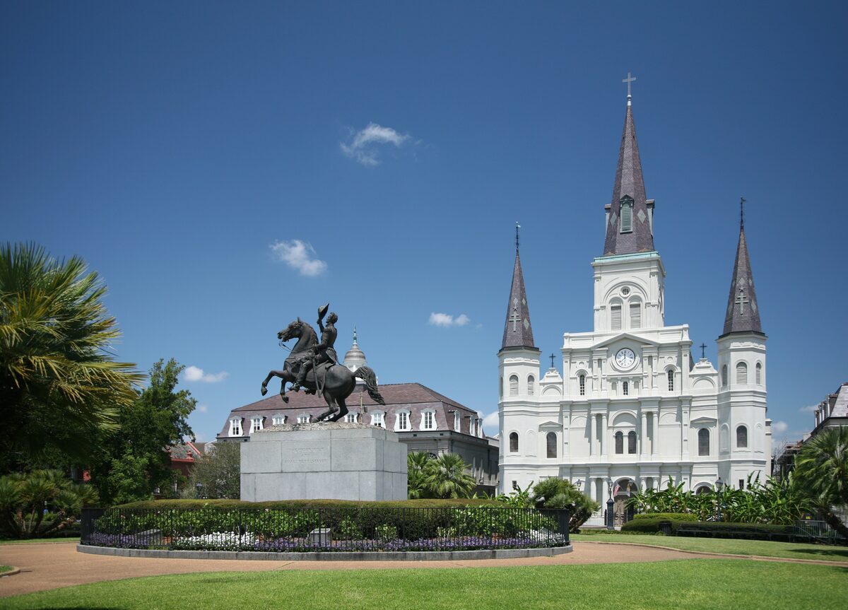 St. Louis Cathedral with its three spires and the equestrian statue of Andrew Jackson in the green square, under a blue sky