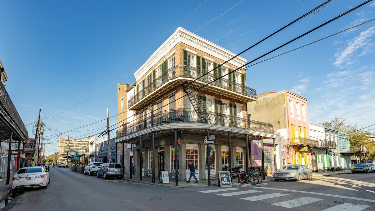 A corner building with iron galleries on a street in Faubourg Marigny, with colorful houses further down the block