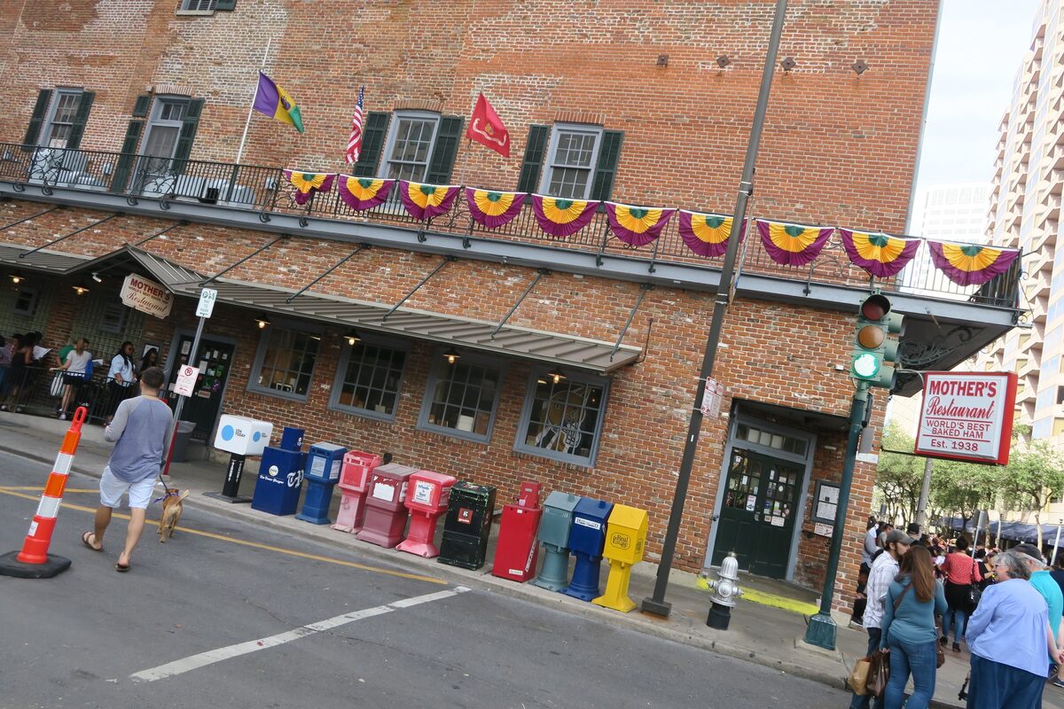 The brick corner building of Mother's Restaurant with its red sign, a balcony hung with bunting and people queuing on the pavement