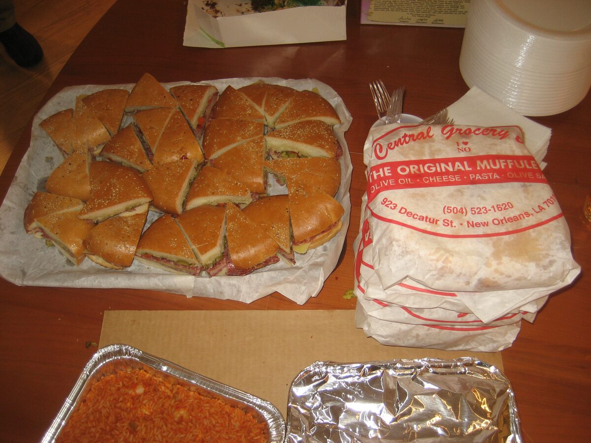 A muffuletta cut into wedges next to its paper wrapping from Central Grocery