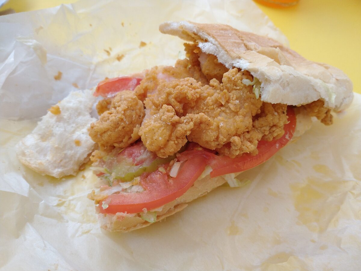 A fried shrimp po'boy dressed with tomato and lettuce, half unwrapped from its paper