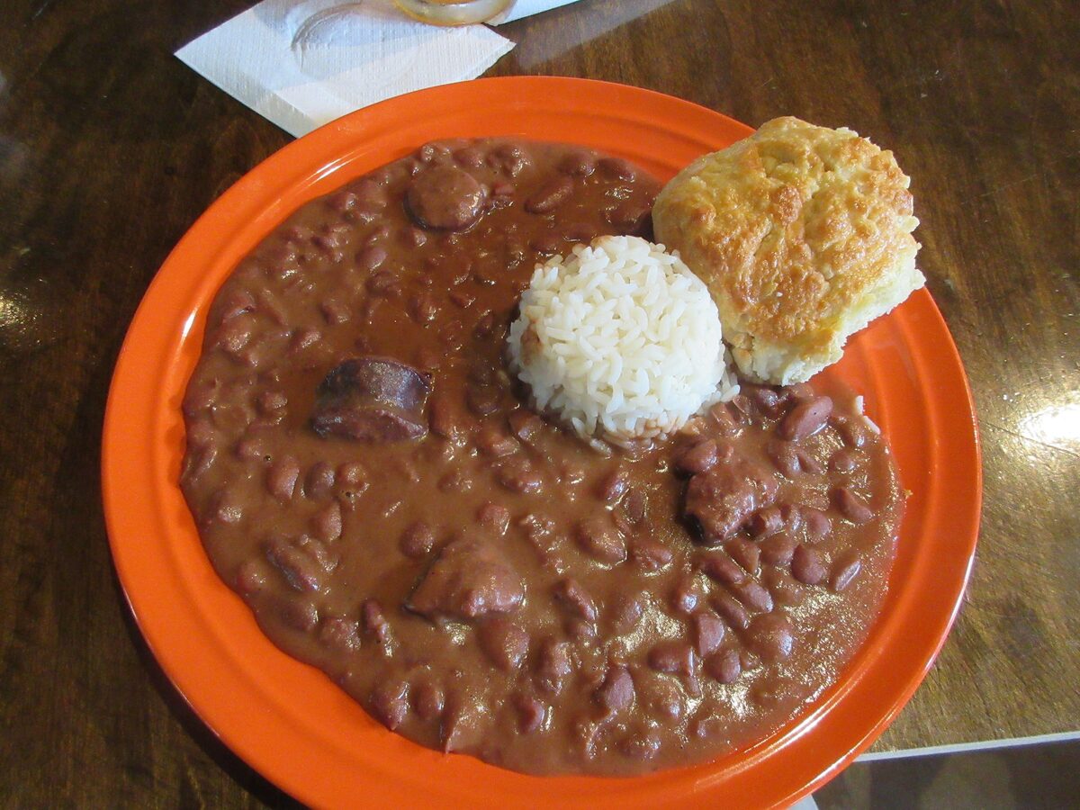 A plate of red beans with sausage, a scoop of rice and a cornbread muffin on an orange plate