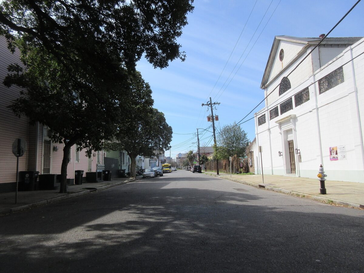 The plain white front of St. Augustine Church at the end of a quiet Tremé street under a blue sky