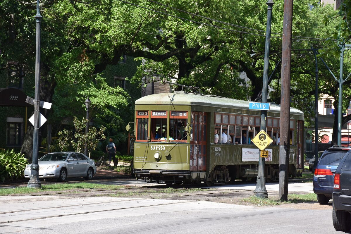 A green St. Charles streetcar rolling past live oaks and houses on St. Charles Avenue