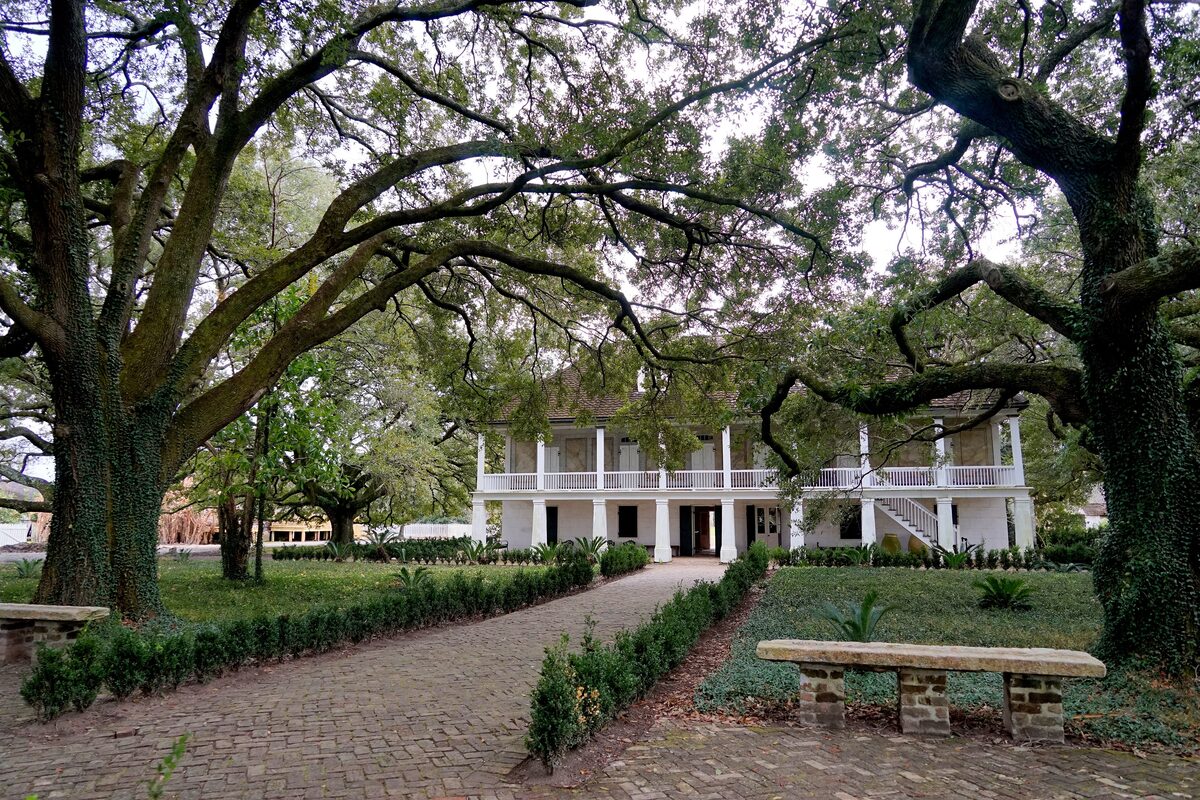 The white-columned Big House of Whitney Plantation seen along a brick path between live oaks