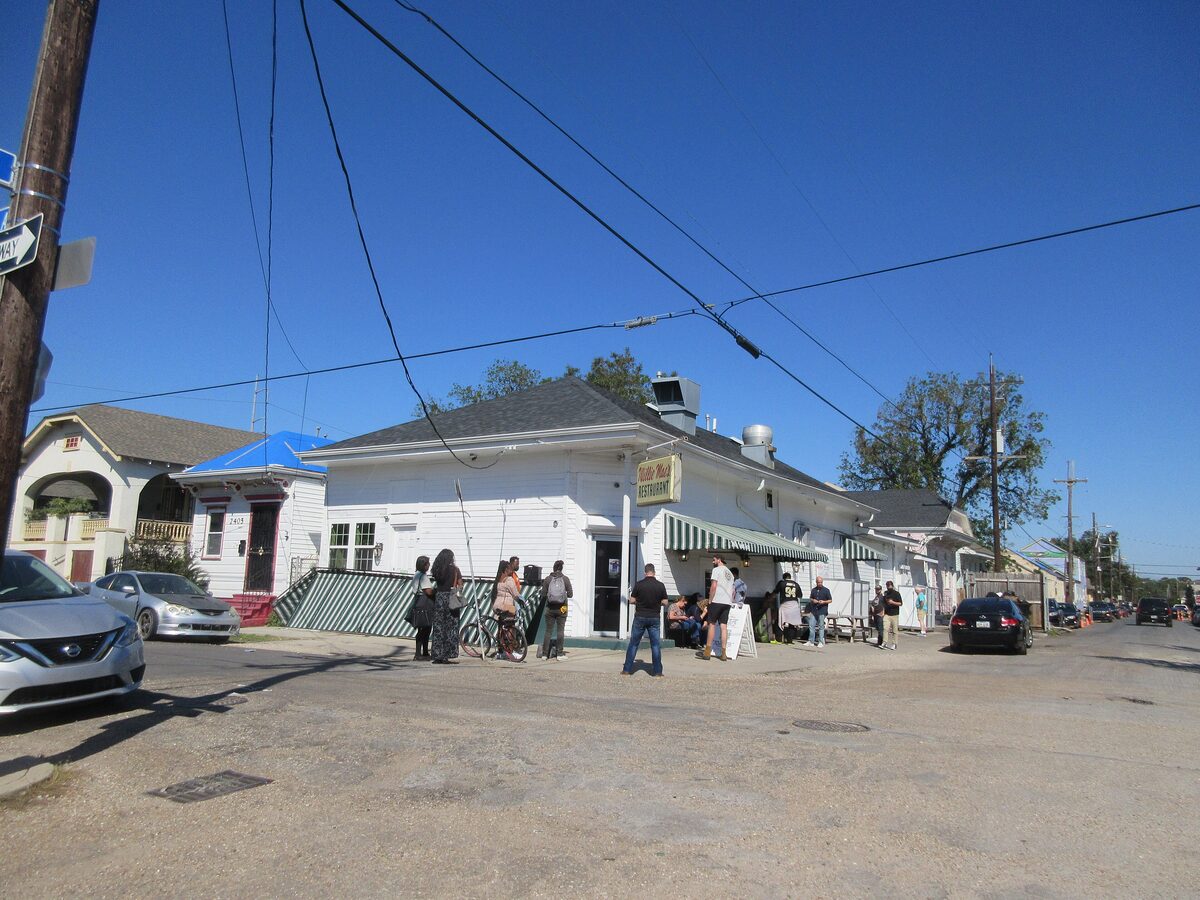 Diners waiting outside the low white Willie Mae's Scotch House building on a sunny corner in Tremé