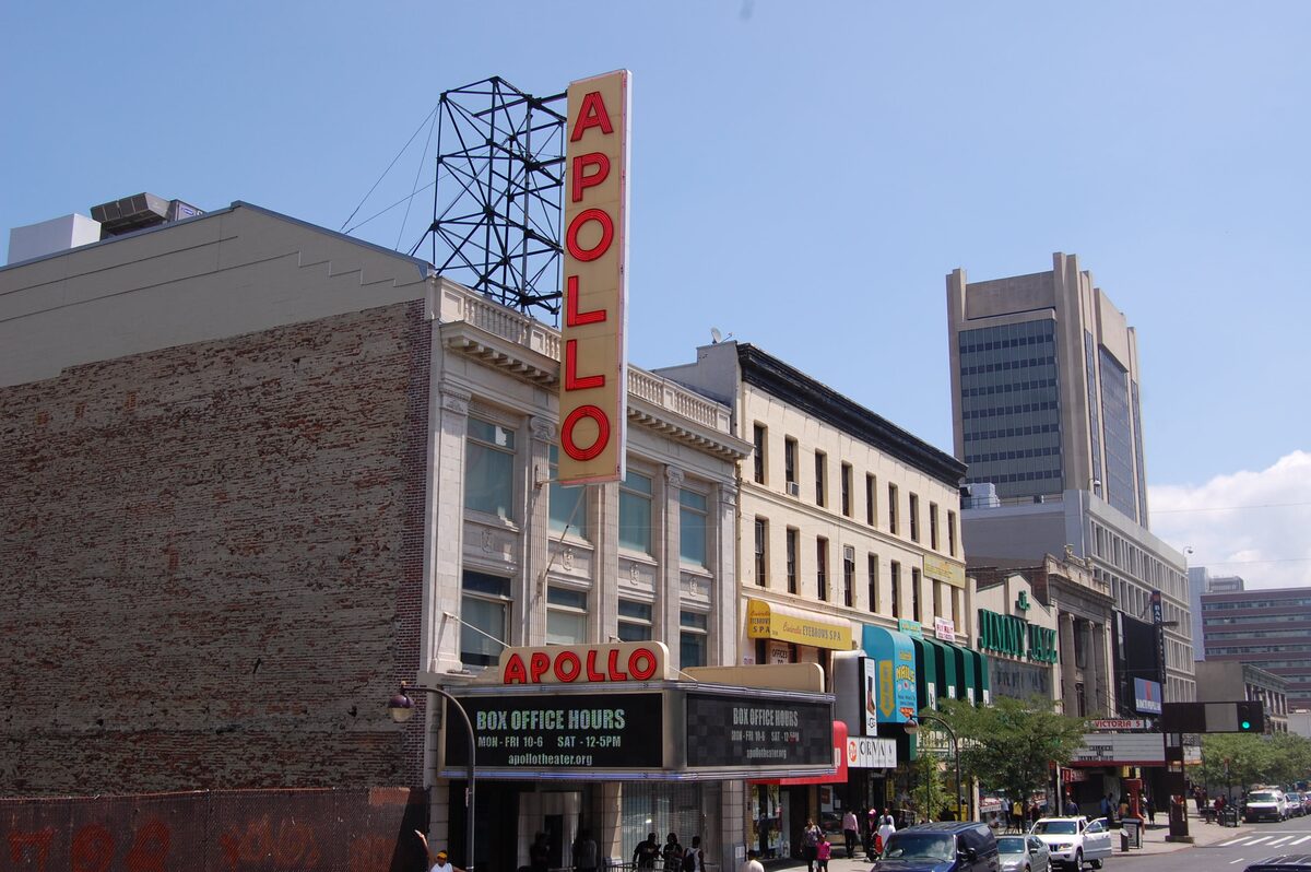 The tall red vertical Apollo sign and the marquee of the Apollo Theater on 125th Street in daylight