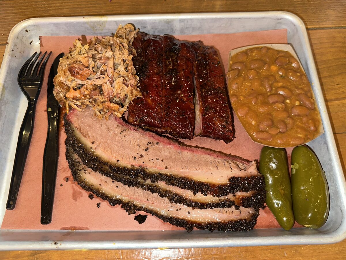 A tray of sliced Texas-style brisket, pork ribs, pulled pork, beans and pickled jalapenos