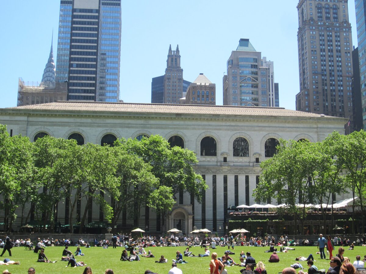 People sunbathing on the green lawn of Bryant Park with the back of the New York Public Library and Midtown towers behind