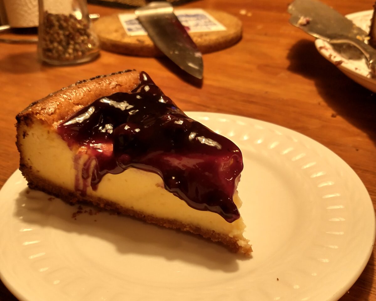 A slice of New York cheesecake with blueberry topping on a white plate