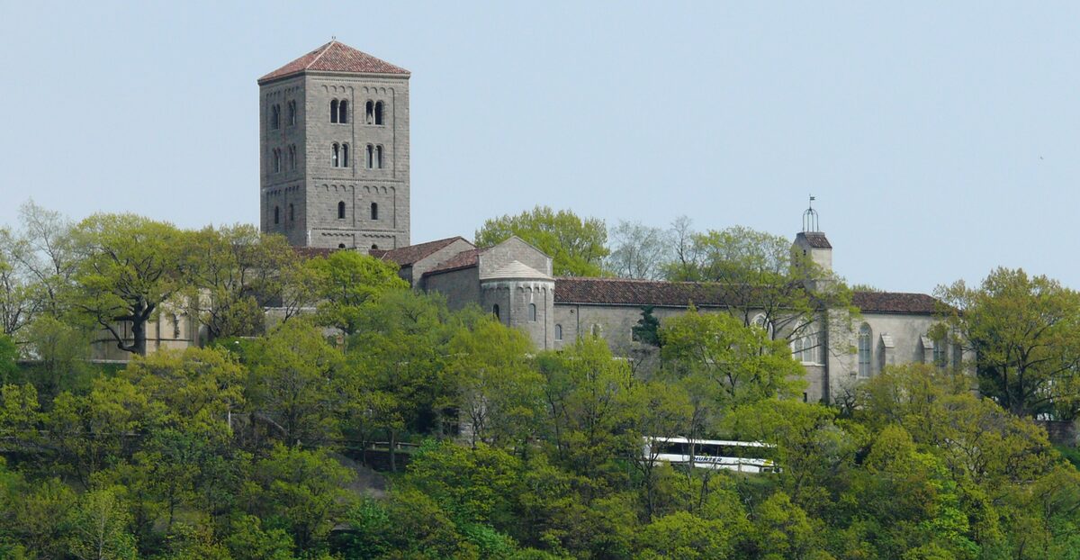 The stone tower and walls of the Met Cloisters on a wooded hill above the Hudson River