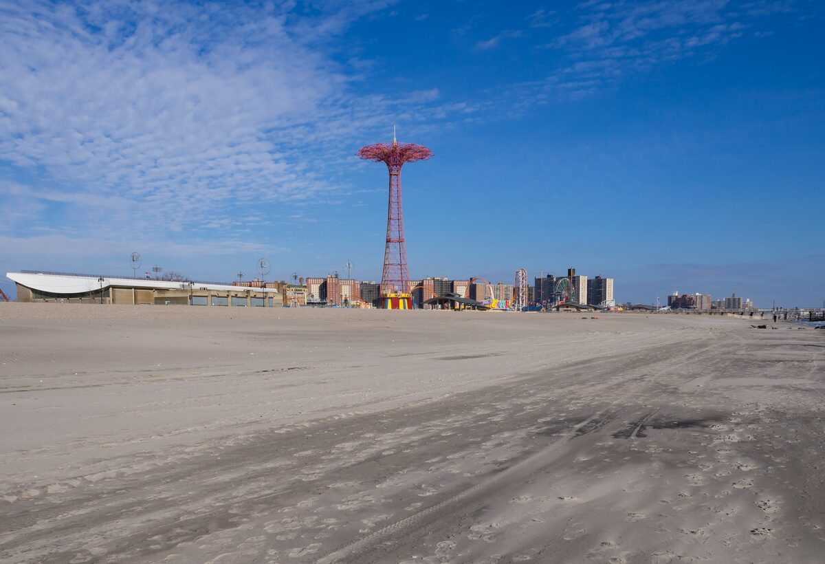 The wide sandy beach at Coney Island with the Parachute Jump tower and the amusement area on the horizon