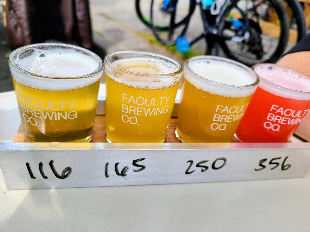 A flight of four small glasses of craft beer, from pale gold to red, on a tasting paddle