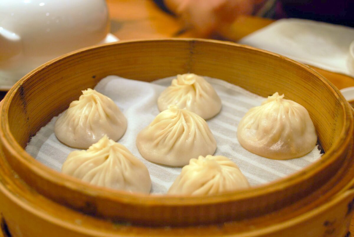 Five soup dumplings (xiao long bao) in a bamboo steamer basket lined with paper