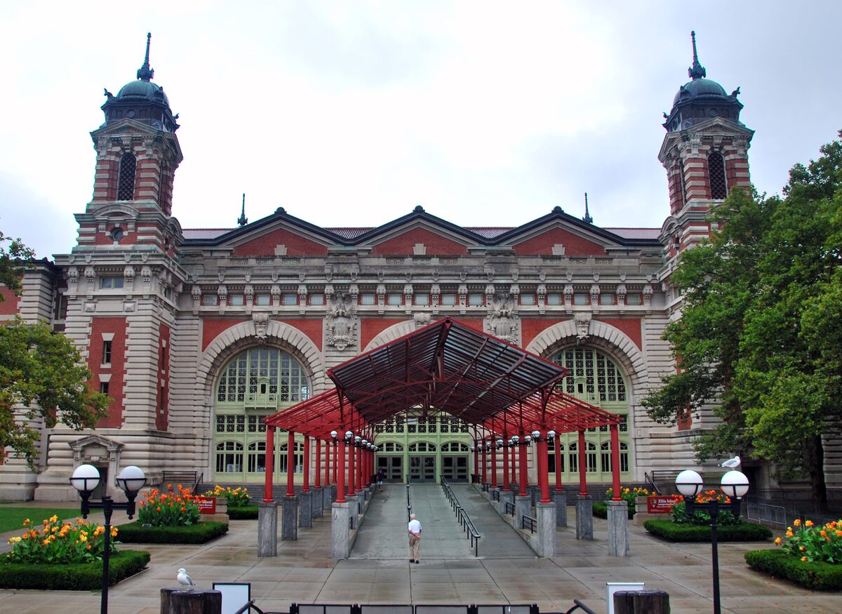 The red-brick and limestone Main Building of the Ellis Island Immigration Museum with its four towers and a red canopy walkway