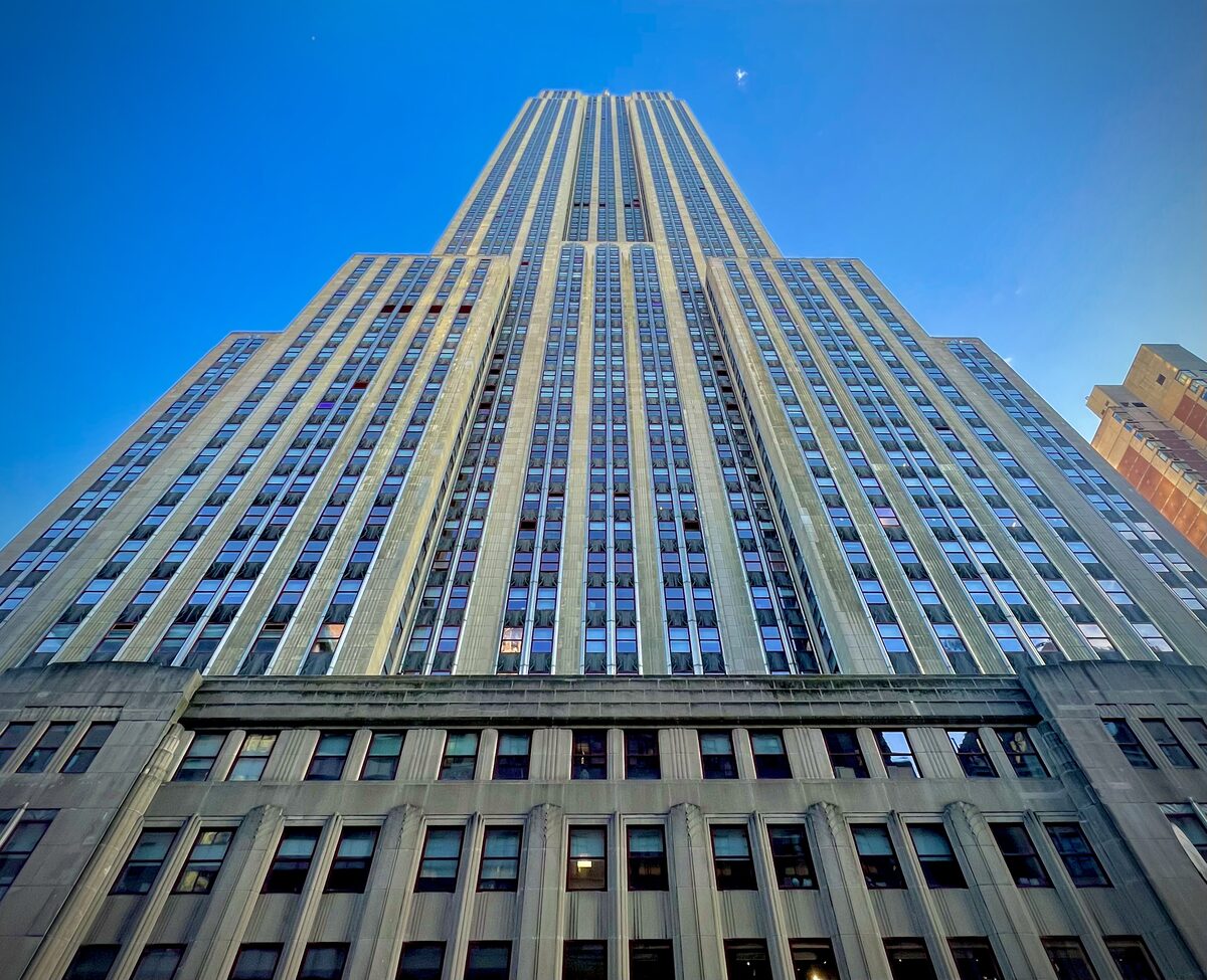Looking straight up the limestone and steel Art Deco tower of the Empire State Building against a deep blue sky