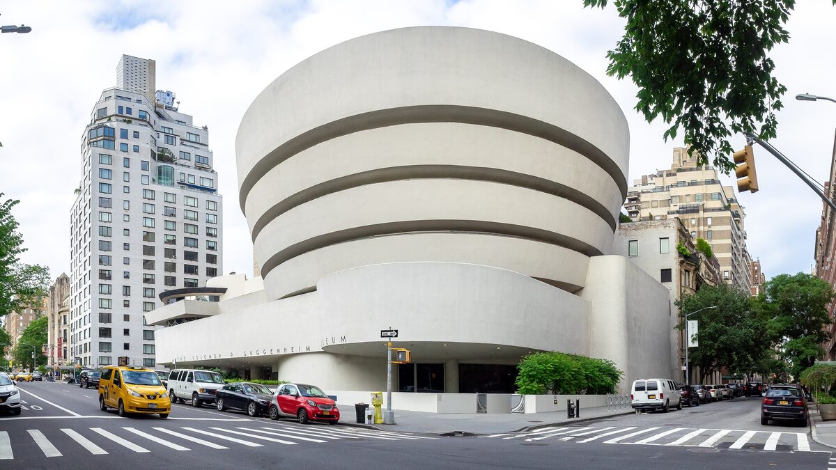 The white spiral rotunda of the Guggenheim Museum on Fifth Avenue seen from the corner, with a yellow taxi in the street