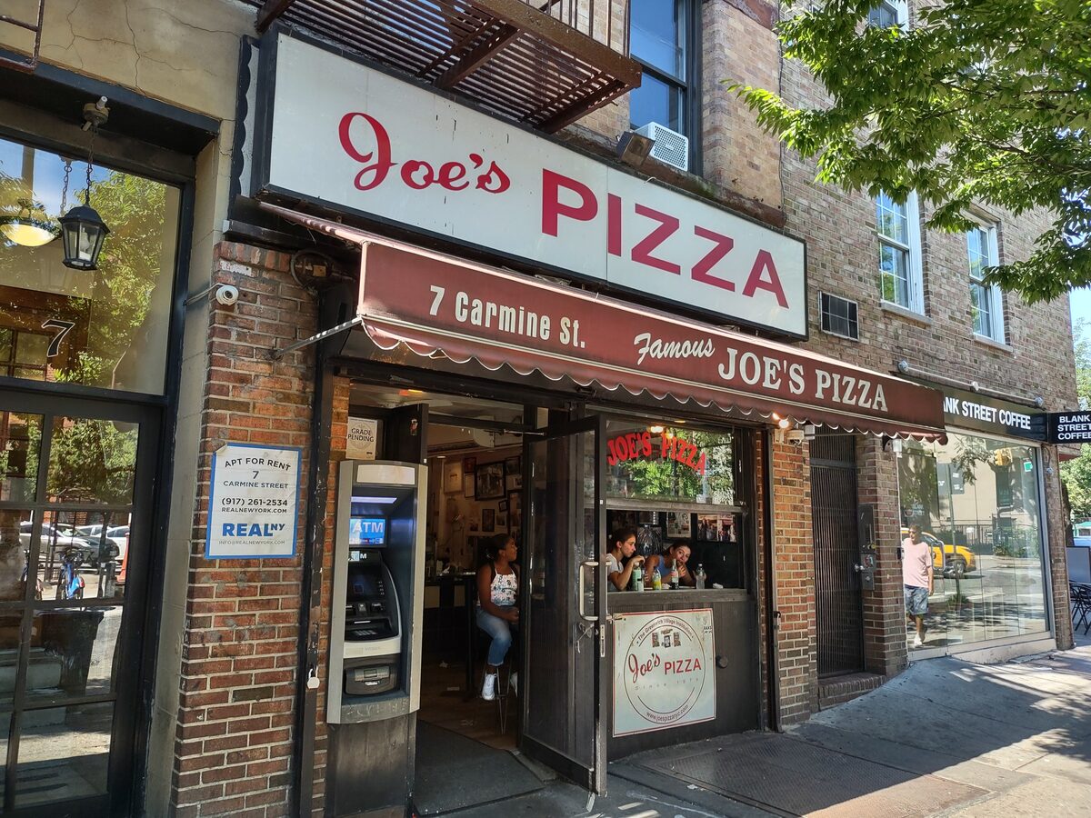 The storefront of Joe's Pizza at 7 Carmine Street with its red-script sign and awning