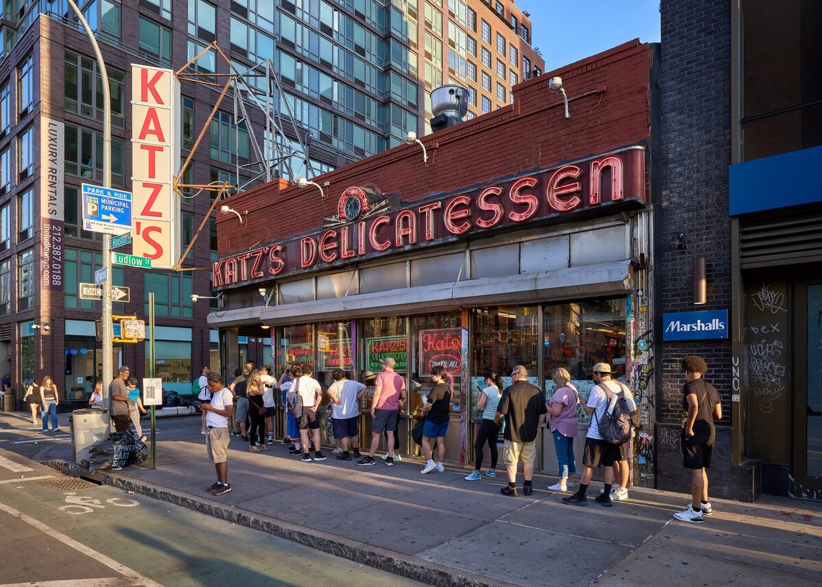 The red neon Katz's Delicatessen sign over the corner shop on Houston Street, with a line of people waiting outside