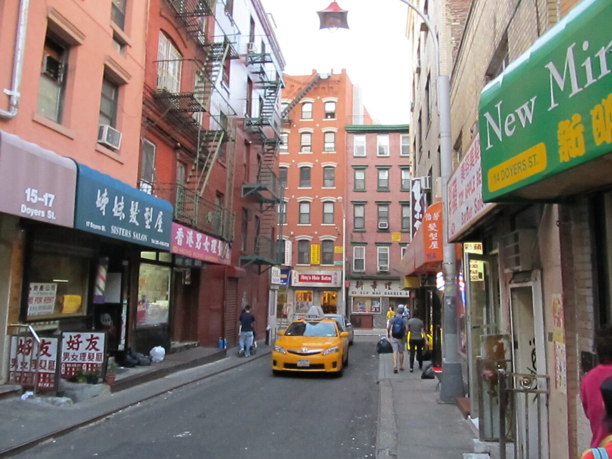 Doyers Street in Chinatown, the short bent lane lined with red-brick buildings and Chinese shop signs, with a yellow taxi in the distance