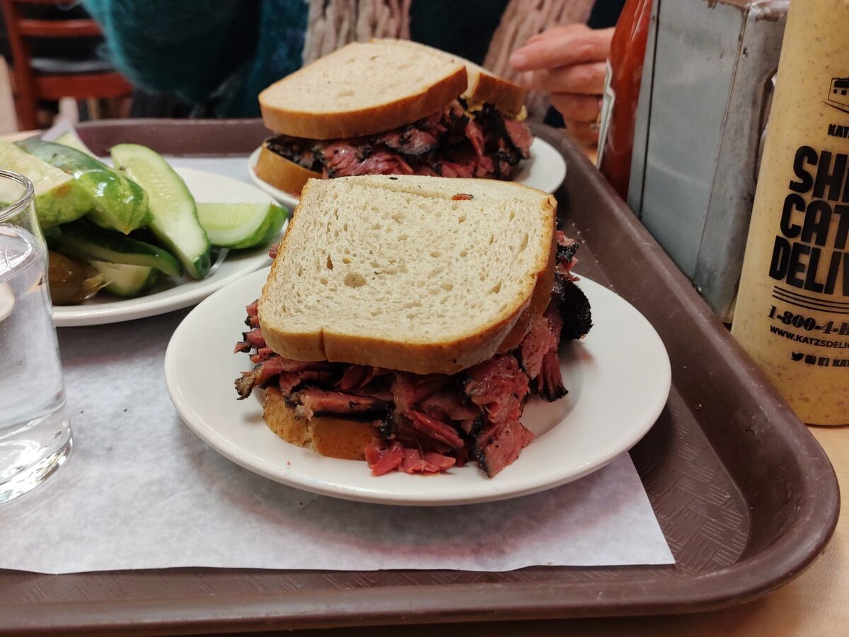 Two halves of a pastrami sandwich on rye bread piled high on a plate on a cafeteria tray at Katz's