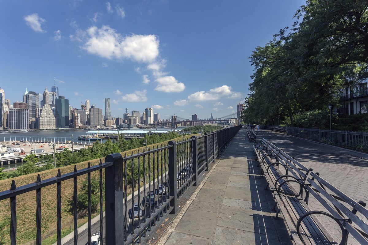 The Brooklyn Heights Promenade with its railing and benches and the Lower Manhattan skyline across the East River