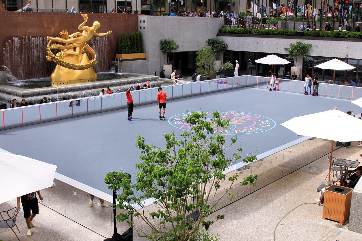 The golden Prometheus statue over the Lower Plaza of Rockefeller Center, with the skating rink below and umbrellas around it