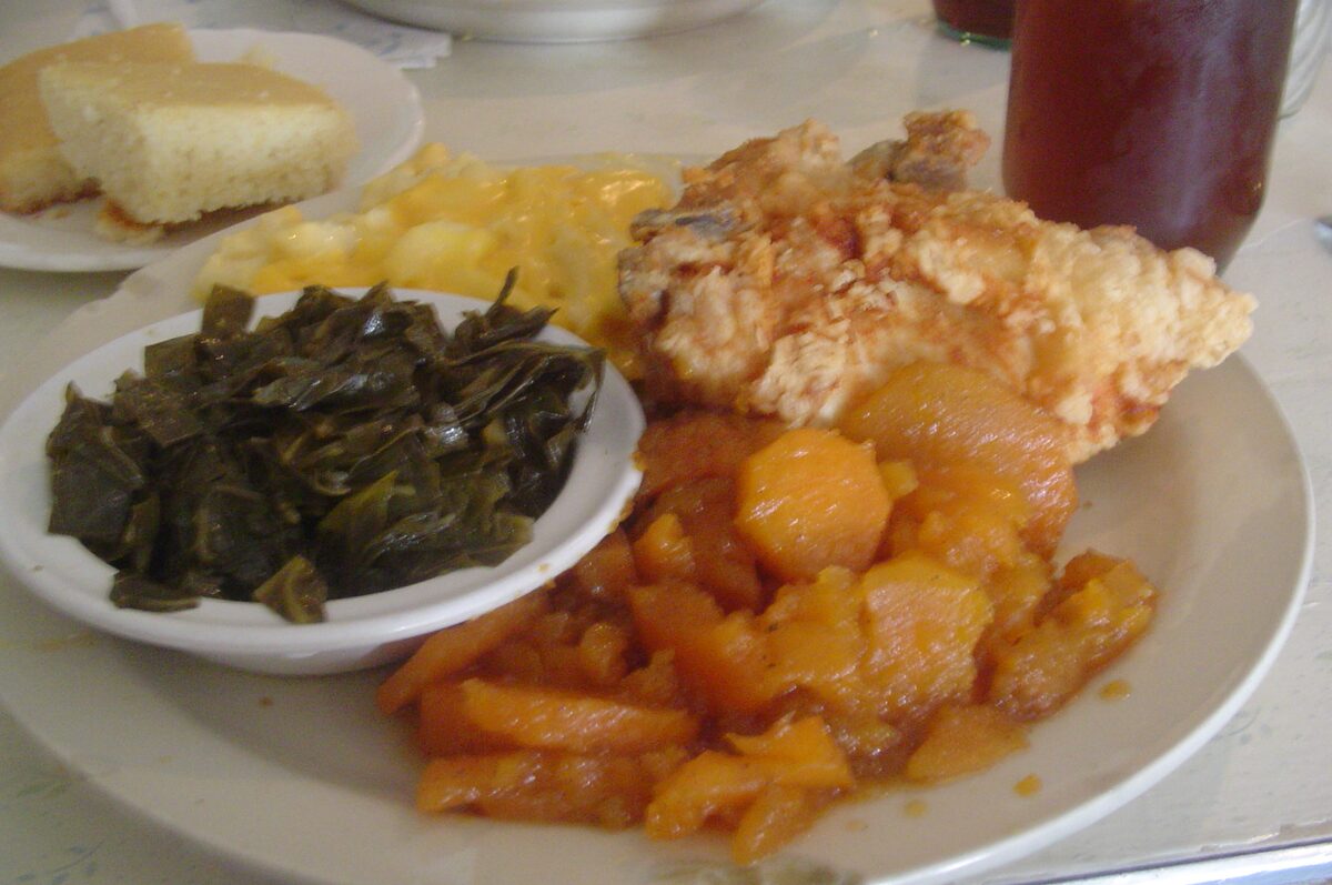 A soul food plate with fried chicken, collard greens, candied yams and cornbread