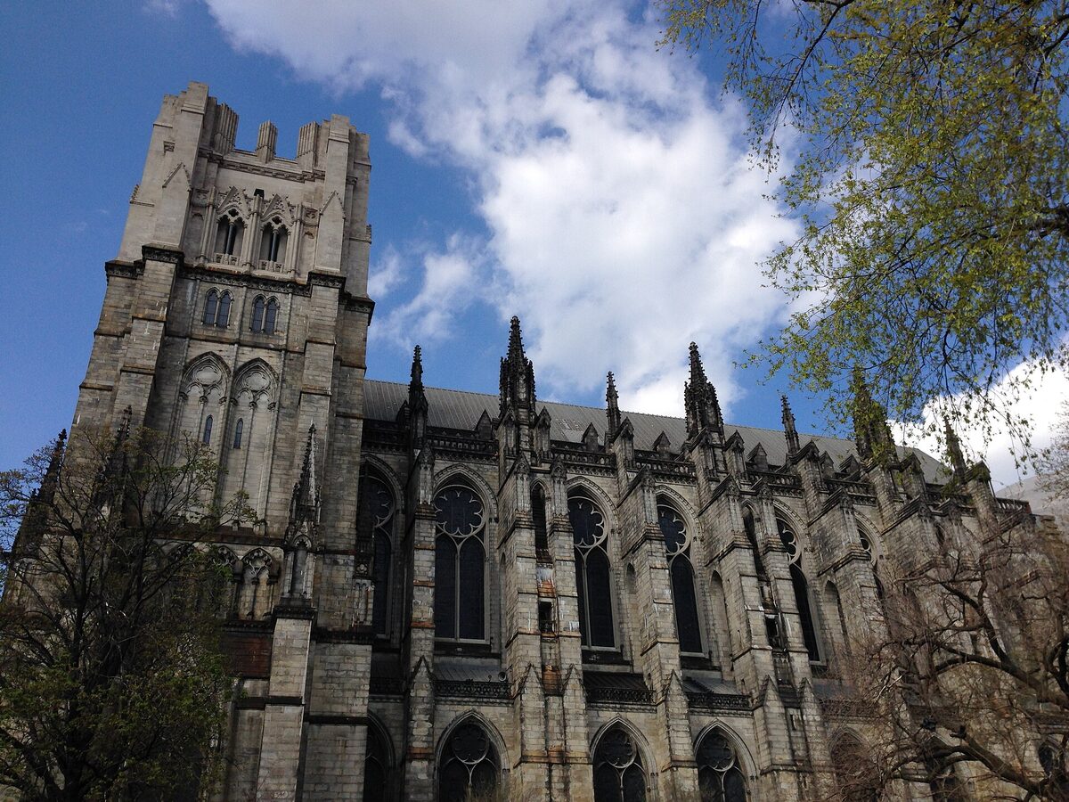 The Gothic stone nave and towers of the Cathedral of St. John the Divine seen from the side against a blue sky