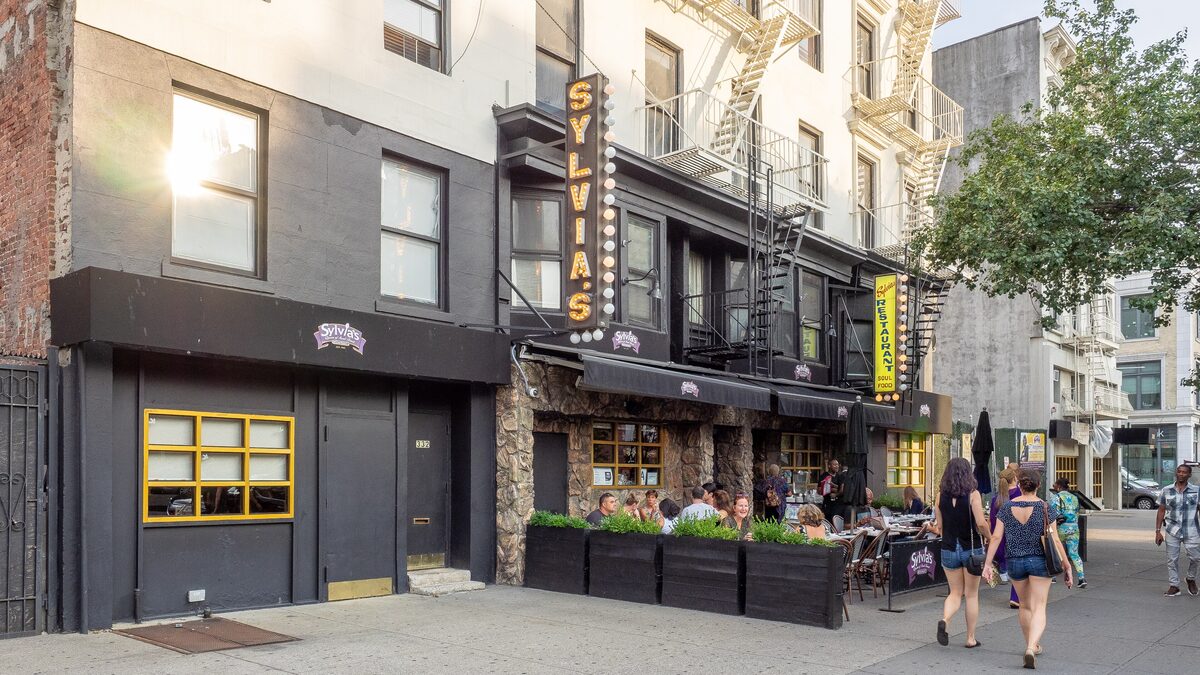 The yellow vertical Sylvia's sign over the restaurant's sidewalk terrace on Malcolm X Boulevard in Harlem